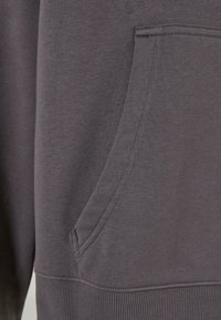 Grå sweatshirtstoff med en myk tekstur, med en sidelomme og ribbestrikkede mansjetter i kanten. Ingen synlige mønstre eller dekorasjoner.