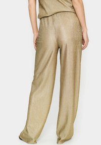 Złote, żebrowane, szerokie spodnie z elastycznym paskiem w talii i miękką, błyszczącą fakturą. Posiadają luźny krój i sięgają do kostek.