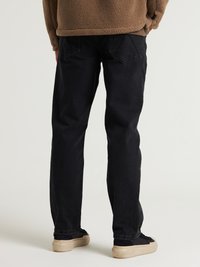 Jeans negros de corte recto, con bolsillos traseros y una tela duradera, combinados con zapatillas negras y una parte superior de forro polar marrón texturizada.