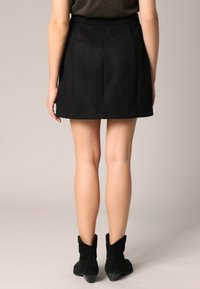 Zwarte suède mini-jurk met een aansluitende taille en uitlopende onderkant; gladde textuur. Draag het met zwarte enkellaarzen, dat een eenvoudige, strakke uitstraling toont.