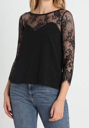 Black top featuring sheer lace long sleeves with floral patterns and a solid black bodice. Round neckline, relaxed fit, and soft texture.