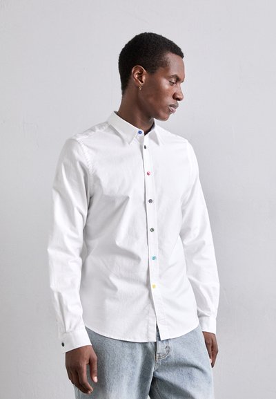 Chemise blanche à manches longues avec boutons multicolores sur le devant et aux poignets. Texture subtile, design de col classique.