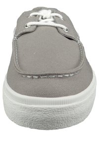 Zapatilla de lona gris con suela de goma blanca, puntera redondeada y cordones blancos. Presenta costuras a lo largo del borde y ojales de metal para los cordones.