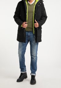 Černá zateplená bunda se zeleným podšívkou, nošená přes zelený svetr, doplněná modrými džínami a černými botami. Obsahuje zipy a kapsy.