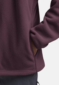 Fleece-Pullover in tiefem Pflaumenfarbton mit strukturierter Oberfläche. Verfügt über eine Seitentasche und gerippte Bündchen für einen snug fit.