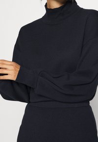 Maglione a collo alto righettato di colore blu navy, con maniche lunghe e vestibilità rilassata. Presenta un colletto alto e una texture morbida per il massimo comfort.