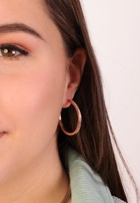 Roze gouden ring oorbel met een dunne, sprankelende accent; gladde oppervlakte; cirkelontwerp; gedragen aan het oor van een persoon.