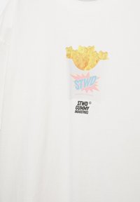 Cămașă albă cu un buzunar plin cu ursuleți gumați galbeni și textul "STWD" și "STWD Gummy Industries" imprimat pe piept.