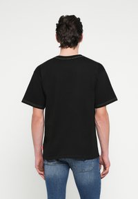 Μαύρο βαμβακερό t-shirt με κοντά μανίκια, στρογγυλή λαιμόκοψη και κίτρινες λεπτομέρειες ραφής. Οπίσθια όψη με απλό σχέδιο και άνετη εφαρμογή.