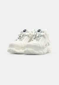 White athletic shoes with textured leather and mesh upper, featuring gray laces, a rounded sole, and a small circular logo on the tongue.