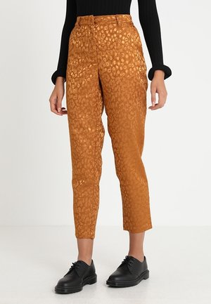 Rostfarbene, gekürzte Hose mit dezentem Animal-Print, kombiniert mit schwarzen Schnürschuhen und einem schwarzen Langarmtop.