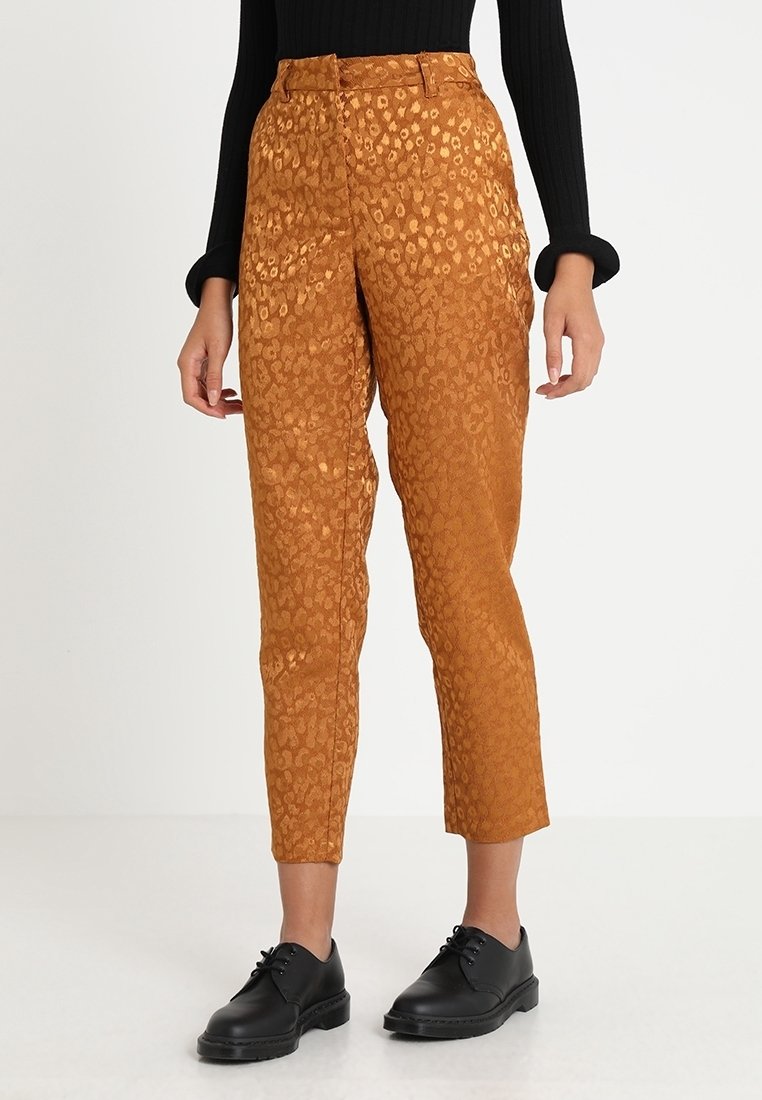 Pantalon court couleur rouille avec un imprimé animalier subtil, porté avec des chaussures noires à lacets et un haut noir à manches longues.