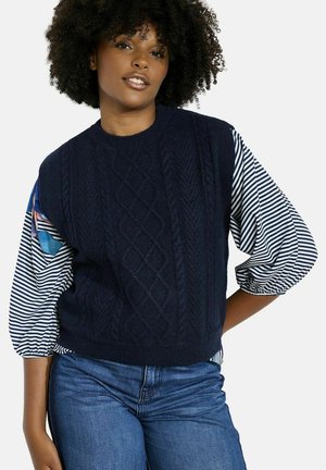 Maglione lavorato a maglia blu navy con un motivo a rombi e orlo a coste, abbinato a maniche a palloncino striate con accenti floreali colorati.