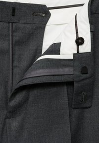 Ciemnoszare spodnie z otwartym zamkiem błyskawicznym, guzikiem i zapięciem, ukazujące białą podszewkę z czarną lamówką.