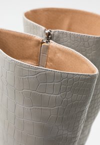 Bottes en cuir gris avec un motif crocodile, dotées d'un intérieur lisse et d'une fermeture éclair en haut.
