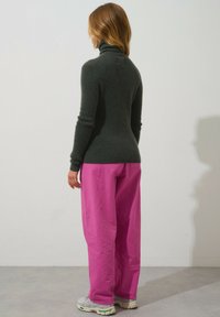 Mörkgrön polotröja med åtsittande silhuett, kombinerad med lösa, ljusrosa byxor som har texturerad tyg och elastisk midja.