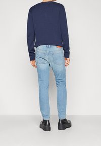 Suéter de punto en color azul marino combinado con pantalones vaqueros de un azul claro. Los pantalones tiene un diseño clásico con bolsillos traseros y detalles de costura sutiles. Botas negras visibles.