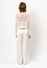 Gebreide, korte trui in lichtbeige met open weefpatroon. Gecombineerd met hoge taille, wijde broek in off-white.
