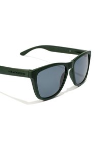 Green sunglasses with a textured matte finish, cat-eye shape, dark lenses, and bold brand logo on the temple.