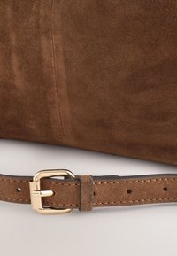 Close-up of brown suede belt with gold-tone rectangular buckle and stitched edges on a matching suede background.