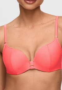 Korallinpunainen rintaliivit, joissa on uritettu rakenne, muotoillut kupit ja säädettävät olkaimet. Keskellä on lukko, jossa on kullanväriset koristeet.