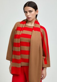 Braun gestreifter Pullover mit roten Akzenten, kombiniert mit einem passenden roten Schal und roten Hosen. Weicher Stoff und entspannte Passform.