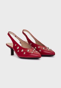 Czerwone skórzane buty na obcasie typu slingback z ostrym noskiem, zdobione metalowymi ćwiekami i niskim obcasem blokowym. Gładka tekstura, minimalistyczny design.
