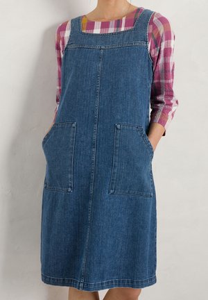 Denim-overallskjole med firkantet udskæring og to store forlommer. Designet har en tætsiddende overdel og et skørt, der flænger ud.