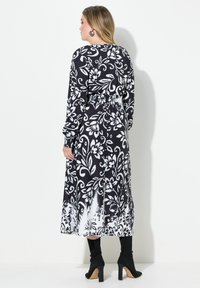 Lång svart och vit blommig klänning med långa ärmar, cinchad midja och en flödig kjol; textil med en djärv mönstring. Matchad med svarta klackstövlar.