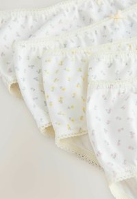 Vier witte katoenen damesonderbroeken met kleine blauwe, gele en roze bloemenprints en kanten afwerking, overlappend gerangschikt op een lichte ondergrond.
