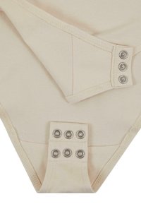 Nude színű anyagú bodysuit, amely alul csattal záródik, puha tapintású és tiszta varrásokkal rendelkezik. Kb. háromszögletű forma.