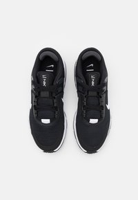 Zapatillas deportivas negras hechas de malla y materiales sintéticos, con acentos blancos, diseño con cordones y un collar acolchado para mayor comodidad.