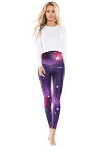 Langärmliges weißes Oberteil kombiniert mit lila Leggings im Galaxy-Muster, die Sterne und einen strukturierten Bund haben. Die Leggings zeichnen sich durch lebendige Farben und Details aus.