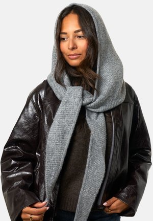 Lichtgrijze, textuurdoek gewikkeld om het hoofd en de nek, gecombineerd met een glanzende bruin leren jas en een donkere trui.