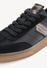 Sneaker nera con tomaia in nubuck e pelle, dettagli laterali grigi, lacci piatti e suola in gomma color gum. Presenta un dettaglio con logo sul lato.