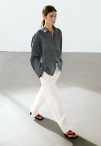 Navy striped button-up shirt with loose sleeves paired with white pinstriped trousers and black flip-flops with red accent straps.