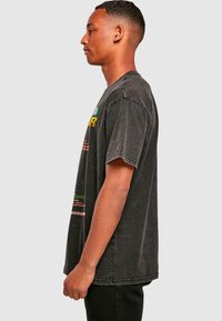 Black oversized denim t-shirt with a relaxed fit, short sleeves, and colorful graphic print on the front. Raw hem detail at the neckline.