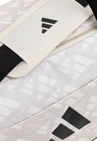 Borsa da viaggio bianca con texture e dettagli neri, dotata di un audace logo nero e chiusura con zip. Il materiale sembra durevole e resistente all'acqua.