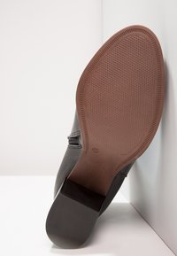 Zapato gris con material superior texturizado, suela de goma marrón plana y un diseño minimalista. Muestra un sutil indicador de tamaño "37".