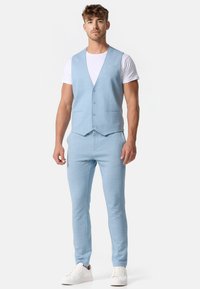 Light blue vest and matching pants made of a soft, textured fabric. Vest features five buttons and two front pockets. White sneakers complete the look.