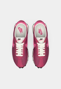 Nike tenisky v tmavě růžové a fuchsiové barvě, s texturovaným svrškem, bílými tkaničkami a logovými akcenty na jazyku a stélce.