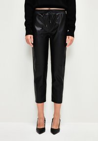 Zwarte leren look, cropped broeken met een elastische tailleband en trekkoord. Gladde textuur, met een naaddetail aan de voorkant.