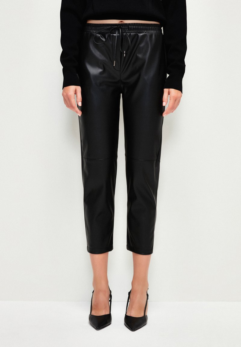 Zwarte leren look, cropped broeken met een elastische tailleband en trekkoord. Gladde textuur, met een naaddetail aan de voorkant.