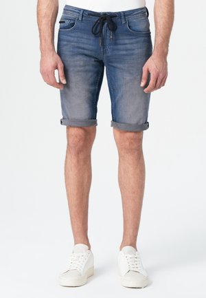 Shorts en denim bleu clair, avec une taille à cordon de serrage, des ourlets roulés et un délavage subtil. Associés à des baskets blanches.