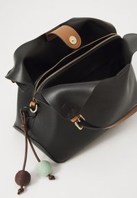 Sac à main en cuir noir avec une texture douce, accents en cuir beige et fermeture éclair dorée. Il comporte des tirettes en pompon colorées et décoratives et un intérieur spacieux.