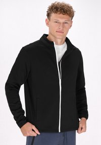 Giacca nera con zip, colletto alto, dotata di zip bianca, tasche laterali e un tessuto liscio e traspirante. Adatta per l'abbigliamento casual.