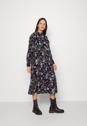 Vestido de manga longa com estampa floral num fundo azul marinho escuro, com bainha ondulada, combinado com botas de tornozelo castanhas com sola grossa.