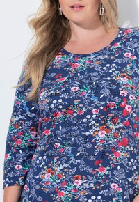 Marinebluse mit Dreiviertelärmeln, verziert mit weißen und bunten Blumenmustern sowie dekorativen Perlenakzenten auf der Vorderseite.
