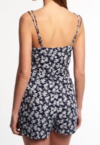 Rompers navy à fleurs présentant des fleurs blanches, des bretelles fines et réglables, un corsage ajusté et un bas court décontracté avec une texture lisse.