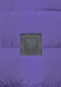 Purple puffer jacket featuring a black branded patch with embossed detail. Smooth texture, stitched sections, and glossy finish.